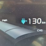 A driver view of an electric car interior with a large touchscreen dashboard showing range and navigation.